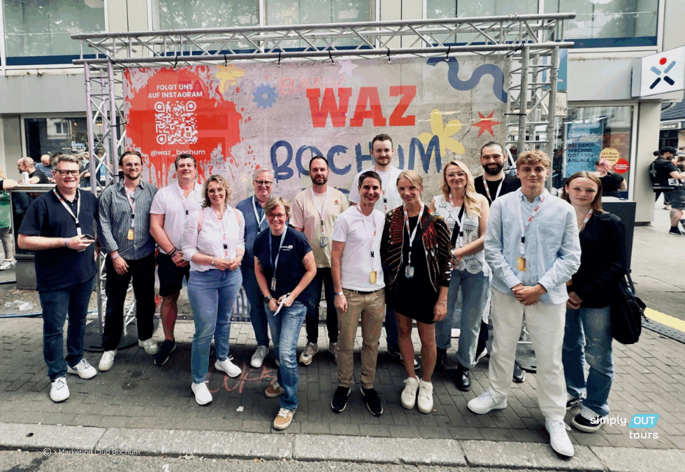 Gruppenfoto vor dem WAZ-Backdrop bei Bochum Total in der Bochumer Innenstadt mit Teilnehmenden einer Backstage-Führung umrahmt von Stadtfest-Stimmung